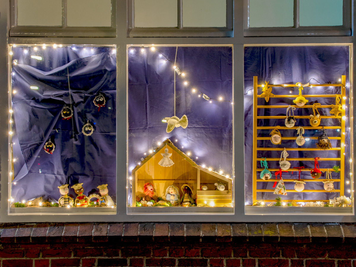 Drie ramen verstuurd met lichtjes. Achter het raam staat een kerststal met gehaakte figuren